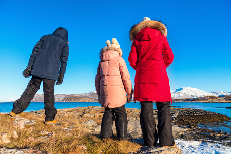 Beautiful family of mother and kids enjoying snowy winter day outdoors at beach surrounded by fjords in Northern Norwayの写真素材