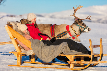 Family of mother and her daughter at reindeer safari on sunny winter day in Northern Norwayの写真素材