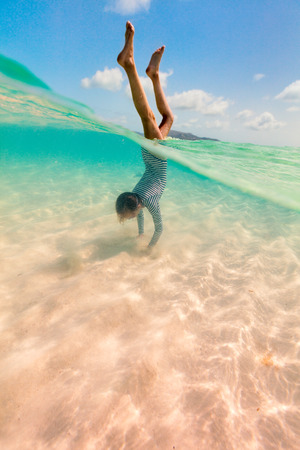 Split underwater photo of little girl splashing in tropical oceanの写真素材