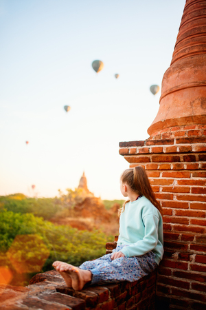 Young girl enjoying rooftop view of hot air balloons fly over thousands of ancient pagodas at sunrise in Bagan Myanmarの写真素材