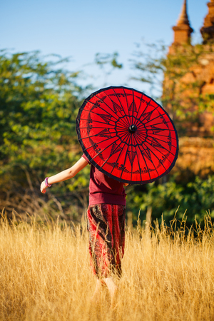 Back view of young girl with traditional burmese parasol visiting ancient temples in Bagan Myanmarの写真素材