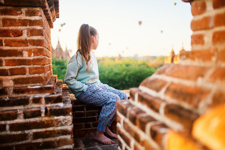 Young girl enjoying rooftop view of hot air balloons fly over thousands of ancient pagodas at sunrise in Bagan Myanmarの写真素材