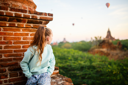 Young girl enjoying rooftop view of hot air balloons fly over thousands of ancient pagodas at sunrise in Bagan Myanmarの写真素材