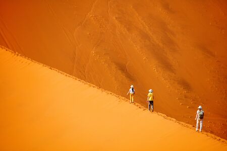 Family of mother and two kids climbing up famous red sand dune Big Daddy in Sossusvlei Namibiaの写真素材