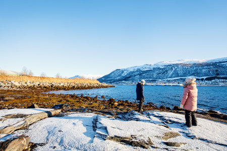 Adorable little girl and cute boy enjoying snowy winter day outdoors at beach surrounded by fjords...