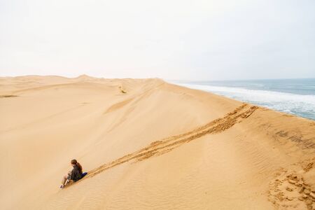 Young girl having fun sliding down from sand dune of Sandwich Harbour in Namibiaの写真素材