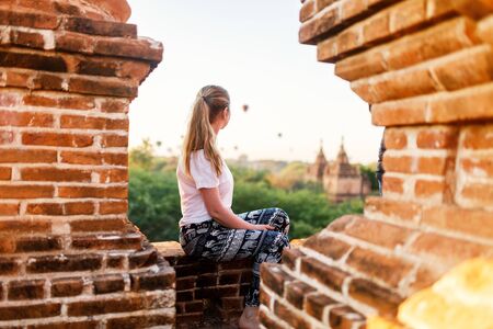 Beautiful woman enjoying rooftop view of hot air balloons fly over thousands of ancient pagodas at sunrise in Bagan Myanmarの写真素材