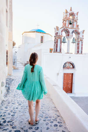Back view of young woman on summer vacation walking near blue domed church in Pyrgos village on Santorini island Greeceの写真素材