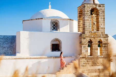 Young girl exploring traditional whitewashed Greek Orthodox church in Plaka village on Milos islandの写真素材