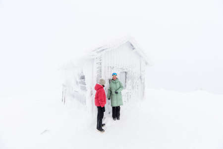 Family of mother and daughter walking next to snow covered hut on winter day in Lapland Finlandの写真素材