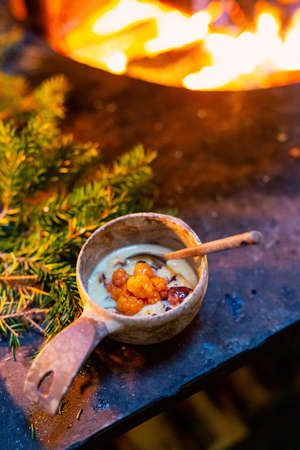 Delicious Lappish baked cheese with cloudberry jam served in wooden bowl in lappish hut next to open fireの写真素材