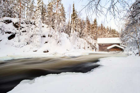 Stunning winter landscape view of snow covered hut by river in Oulanka National Park in Lapland Finlandの写真素材