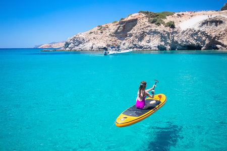 Teenage girl enjoying turquoise waters of Aegean sea in Greece floating on sup during summer vacationの写真素材