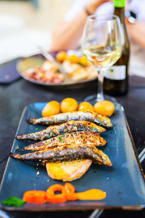 Delicious grilled portuguese sardines served with young potatoes and white wine for lunch or dinner in restaurantの写真素材