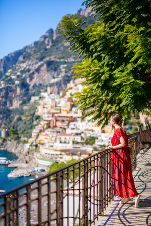 Young woman in red dress enjoying stunning view over Positano town on Amalfi coast in Italyの写真素材