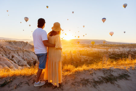 Young romantic couple admire scenery of hot air balloons flying over Love valley with rock formations and fairy chimneys in Cappadocia Turkeyの写真素材