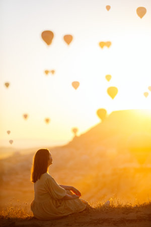 Young woman admire scenery of hot air balloons flying over Love valley with rock formations and fairy chimneys in Cappadocia Turkeyの写真素材