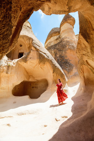 Young beautiful woman in red dress exploring Pasabag Monks valley in Cappadocia Turkey with unique rock formations and fairy chimneysの写真素材