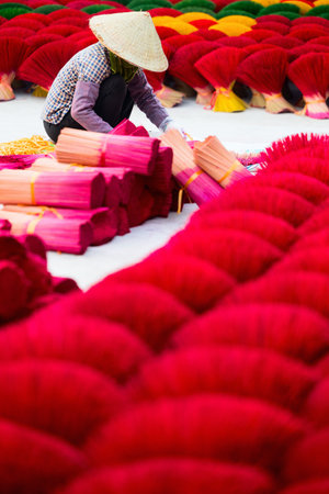 Female worker wearing conical hat among red incense sticks drying outdoor in village near Hanoi in Vietnamの写真素材