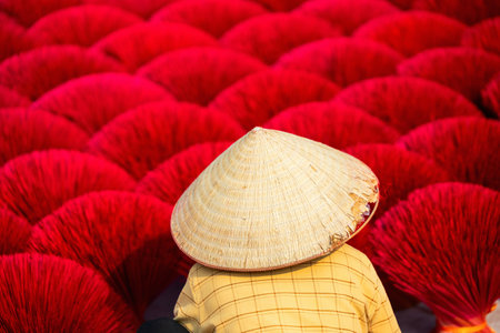 Female worker wearing conical hat among red incense sticks drying outdoor in village near Hanoi in Vietnamの写真素材