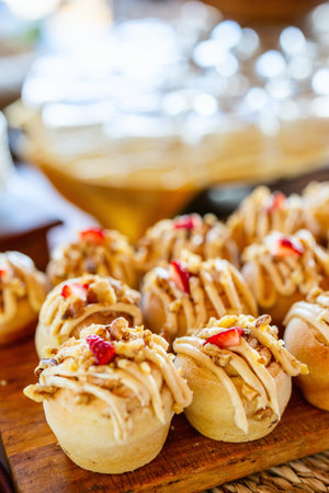 Freshly baked pastries adorned with creamy frosting, chopped nuts, and sliced strawberries,...