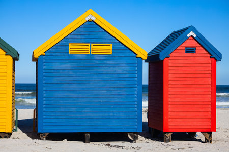 Row of distinctive blue, yellow, red, and green Victorian-style beach changing boxes standing on stilts along Muizenberg&#39;s famous sandy shorelineの写真素材