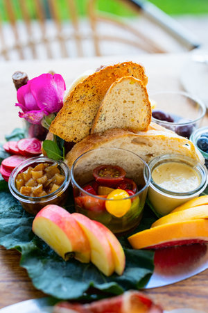 A bright platter showcasing crispy bread slices, sweet chutney, marinated cherry tomatoes, sliced apples, and creamy hummus, elegantly finished with pink beet rounds and a vibrant rose accent.の写真素材