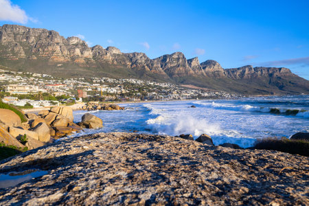 The stunning Cape Town coastline features crashing ocean waves, rocky shores, and the majestic Twelve Apostles mountain range, with a vibrant urban cityscape nestled along the scenic landscape.の写真素材