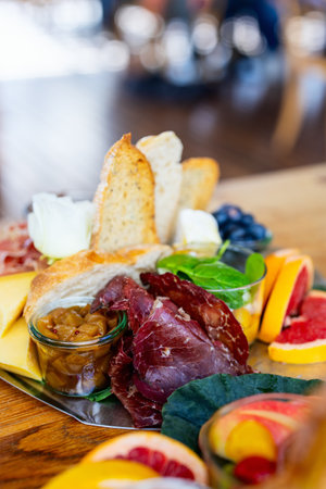 A charcuterie-style arrangement featuring crisp bread slices, flavorful cured meats, tangy cheese wedges, fresh fruit slices, and a sweet chutney, all elegantly accented by a delicate white rose garnish.の写真素材