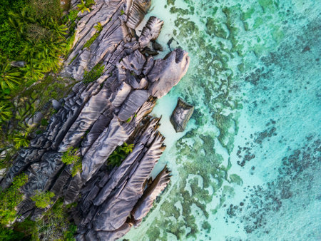 Aerial view of La Digue, Seychelles, featuring striking granite rock formations along the lush shoreline, blending seamlessly with the turquoise waters and coral reef below.の写真素材