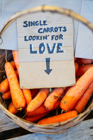 A basket of fresh carrots labeled with a humorous handwritten sign reading â€œSingle carrots...