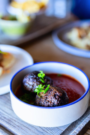Juicy meatballs served in a rich tomato sauce, garnished with fresh green onions, placed in a white bowl with a rustic wooden table background.の写真素材