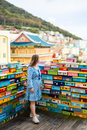 A tourist stands near a colorful installation representing houses in Gamcheon Culture Village, surrounded by vibrant architecture and scenic hillside views.の写真素材