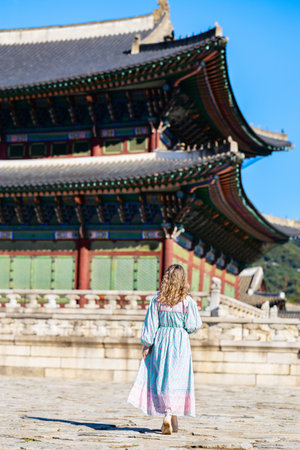 A tourist in a flowing patterned dress explores a historic temple in Seoul, South Korea, with intricate architectural details and vibrant colors in the background.の写真素材
