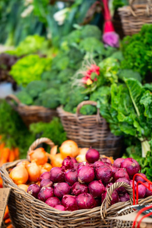 Baskets brimming with red and yellow onions, leafy greens, and other fresh produce at a bustling...