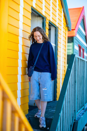 A teenager poses joyfully near vibrant, colorful beach huts at Muizenberg Beach, South Africa, with a relaxed and cheerful expression amidst the iconic architecture.の写真素材