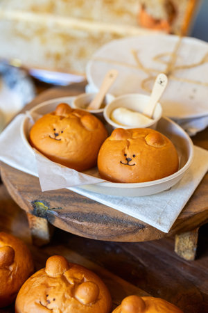 Adorable bear-shaped South Korean salt bread served in a dish with small cups of creamy spread, placed on a rustic wooden surface for a charming presentation.の写真素材
