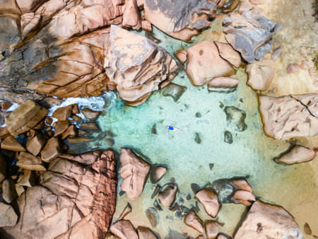 Drone view capturing a woman in a blue swimsuit swimming amidst clear waters and granite rocks at Anse Caiman beach, Seychelles, showcasing tropical beauty and tranquility.の写真素材