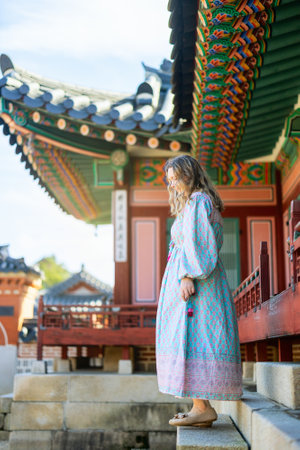 A tourist in a pastel-patterned traditional dress explores a beautifully decorated temple in Seoul, South Korea, surrounded by colorful, intricate eaves and serene architecture.の写真素材
