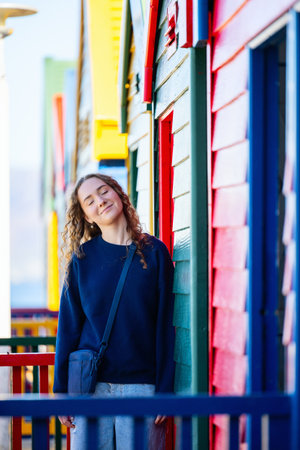 A teenager poses joyfully near vibrant, colorful beach huts at Muizenberg Beach, South Africa, with a relaxed and cheerful expression amidst the iconic architecture.の写真素材