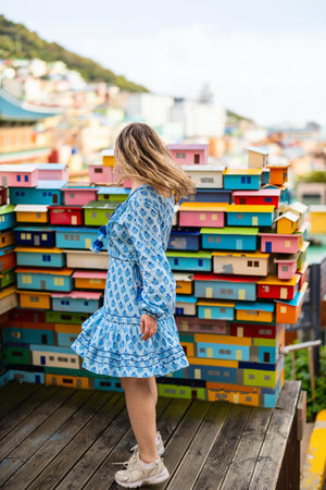 A tourist stands near a colorful installation representing houses in Gamcheon Culture Village, surrounded by vibrant architecture and scenic hillside views.の写真素材