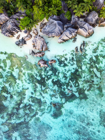 A stunning aerial view of the Seychelles, featuring granite boulders, lush tropical vegetation, and clear turquoise water with intricate reef patterns.の写真素材