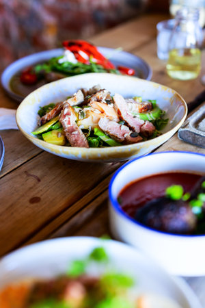 Fresh salad featuring medium-rare sliced duck breast, ripe avocado, mixed greens, and toasted seeds, served in a rustic ceramic bowl on wooden table.の写真素材