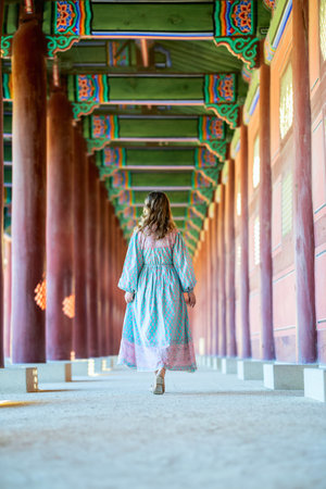 A tourist woman in colorful dress explores the vibrant, intricately decorated interior of a traditional Korean temple in Seoul, South Korea.の写真素材