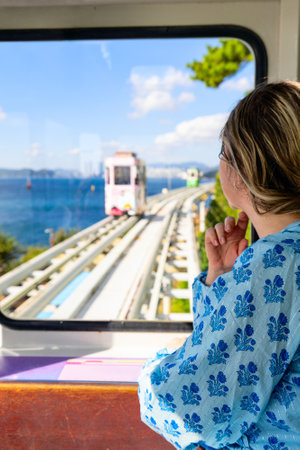 A woman enjoys scenic ocean and rail views in Busan, South Korea, with colorful rail cars visible ahead on a sunny day.の写真素材