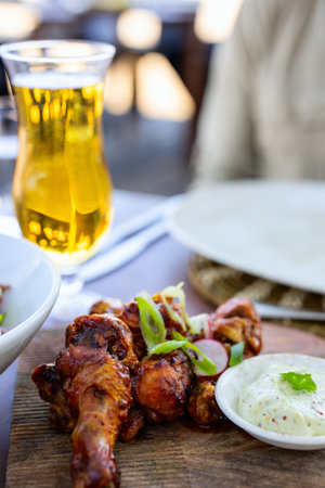 A plate of flavorful grilled chicken wings garnished with green onions and radishes, served alongside a creamy dipping sauce, paired with a refreshing glass of beer.の写真素材