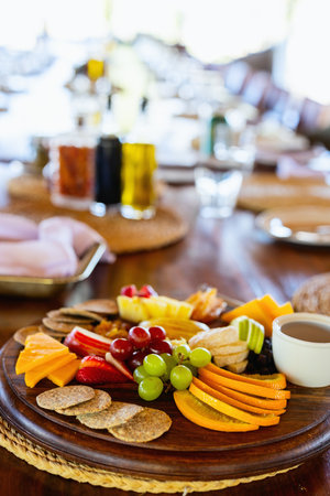A beautifully arranged platter with fresh fruits, cheese, crackers, and dips on a wooden table set for dining, evoking a warm and inviting ambiance.の写真素材