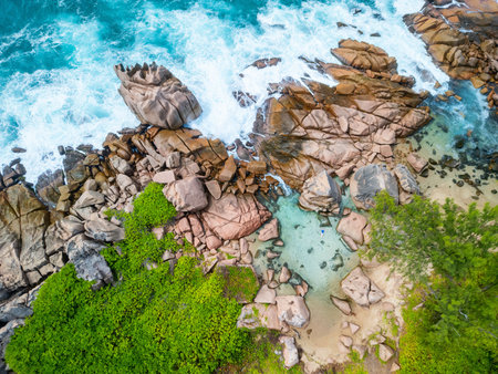 Aerial view of Anse Caiman, Seychelles, showcasing large granite boulders, turquoise waters, lush greenery, and a woman swimming in a shallow natural poolの写真素材