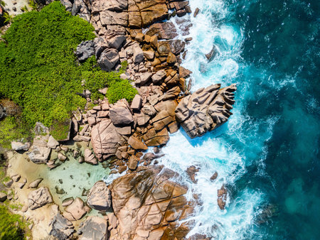 Aerial view of Anse Caiman on La Digue island, Seychelles, featuring rugged granite rocks, clear shallow pools, and vibrant green coastal vegetation along the shorelineの写真素材