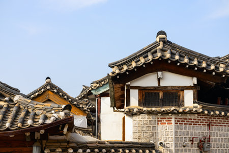 Close-up view of traditional Korean rooftops at Bukchon Hanok Village in Seoul, South Korea, featuring tiled eaves, wooden structures, and stone walls under a clear skyの写真素材